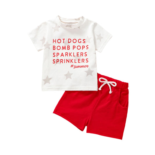 Two piece white and red outfit features a white star print t-shirt with red font that reads, "Hot Dogs, Bomb Pops, Sparklers, Sprinklers, #Summer" on the front with matching solid red elastic shorts with pockets and a white rope-like tie, Jelly Bean Baby Co.